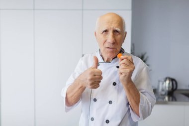 Gri saçlı yaşlı Şef mutfakta bir havuç dilim tatma. Bir havuç ile mutlu bir adam.