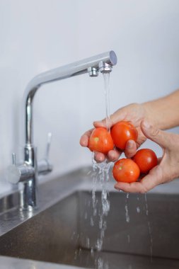 Bir grup bir metal altında kırmızı domates yıkama erkek el mutfak dokunun. Sağlıklı sebze vitaminler tam