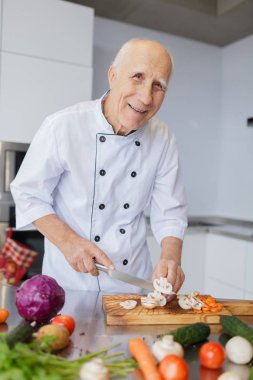 Mutlu yaşlı adam mutfakta yemek yapıyor. Büyükbabam bir bıçak ile bir salata sebze dilimleme. Pişirme kavramı.