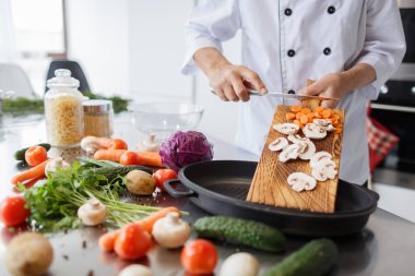 Adamın elleri bir ahşap tahta bir akşam yemeği için havuç ve mantar Dilimleme bir bıçakla. Sebzeler vitamin dolu