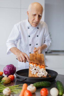 Mutlu yaşlı adam mutfakta yemek yapıyor. Büyükbabam bir bıçak ile bir salata sebze dilimleme. Pişirme kavramı.