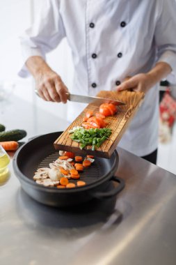 Domates ve yeşil soğan bir ahşap tahta bir akşam yemeği için dilimleme bir bıçakla adamın elleri. Sebzeler vitamin dolu