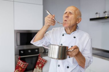 Gri saçla yaşlı adam önce pişmiş bir çorba lezzetli. Dedesi bir metal kaşık ve pan mutfakta