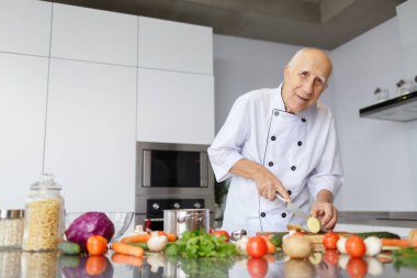Bir huysuz yaşlı adam şef ışık mutfakta bir bıçak kesme patates ile. Bir akşam yemeği için sebzeleri Dilimleme bir kavram.
