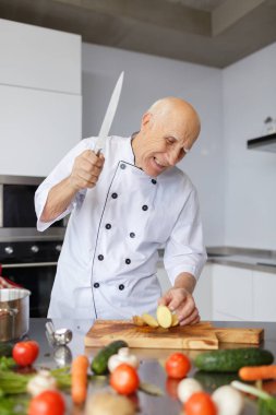 Bir huysuz yaşlı adam şef ışık mutfakta bir bıçak kesme patates ile. Bir akşam yemeği için sebzeleri Dilimleme bir kavram.