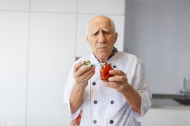 Kırmızı sıcak biber biber ile bir kavanoz mutfak tutan yaşlı bir profesyonel şef portresi. Pişirme kavramı.