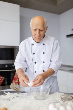 Yaşlı adam şef mutfak cam kasede yumurta böler. Pişirme için çiğ hamur hazırlama unu yemek.