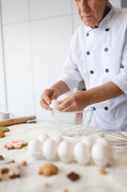 Yaşlı adam şef mutfak cam kasede yumurta böler. Pişirme için çiğ hamur hazırlama unu yemek.
