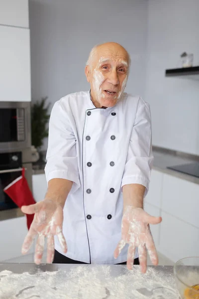 Elderly man chef kneading the dough in the kitchen. Cook in flour preparing raw dough for handmade pizza.