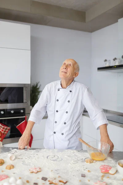 Elderly man chef kneading the dough in the kitchen. Cook in flour preparing raw dough for pizza.