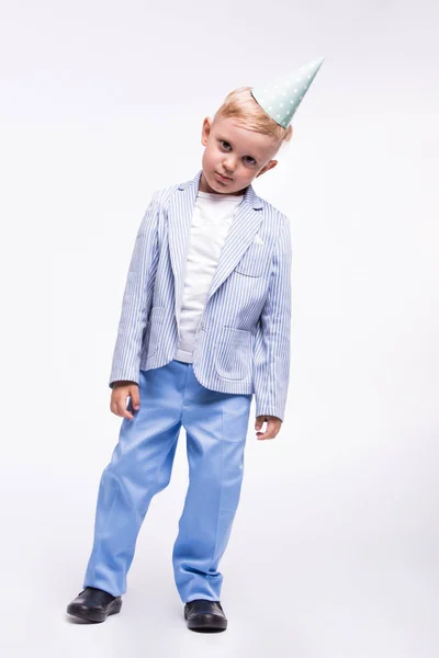 Een kleine schattige jongen in een blauwe pak en op een verjaardag hoed, geïsoleerd op een witte achtergrond. Gelukkige verjaardag-concept — Stockfoto