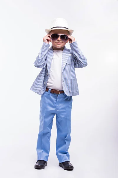 Um rapazinho feliz com óculos de sol, um chapéu e um fato de moda isolado num fundo branco. Conceito de moda infantil — Fotografia de Stock