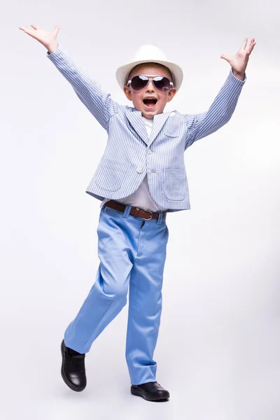 Счастливый маленький мальчик в солнечных очках, шляпе и в модном костюме, изолированном на белом фоне. Забавная детская идея — стоковое фото