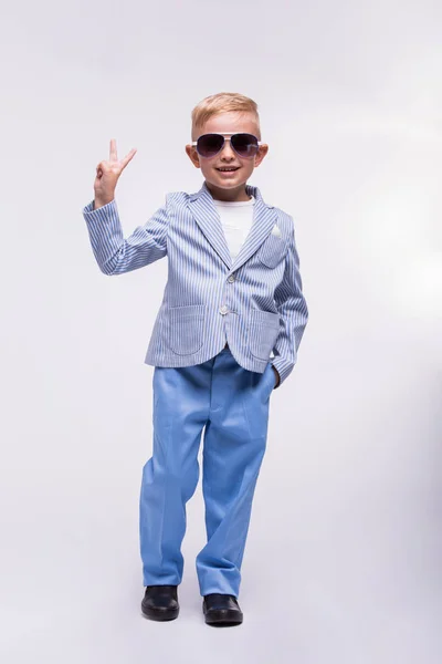 Un niño feliz con gafas de sol y un elegante traje azul aislado sobre un fondo blanco. concepto de moda para niños —  Fotos de Stock