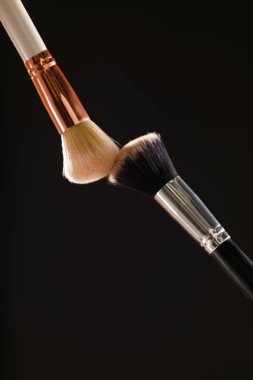 Siyah arka plan üzerine toz allık patlama ile kozmetik fırçalar makyaj