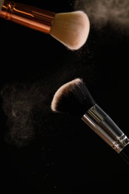 Siyah arka plan üzerine toz allık patlama ile kozmetik fırçalar makyaj