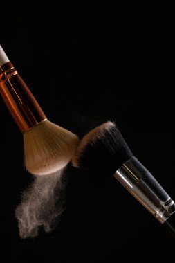 Siyah arka plan üzerine toz allık patlama ile kozmetik fırçalar makyaj