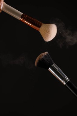 Siyah arka plan üzerine toz allık patlama ile kozmetik fırçalar makyaj