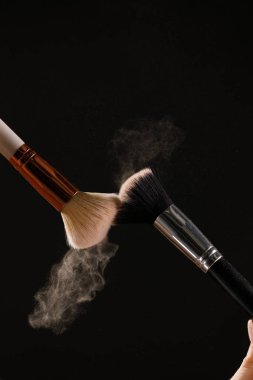 Siyah arka plan üzerine toz allık patlama ile kozmetik fırçalar makyaj