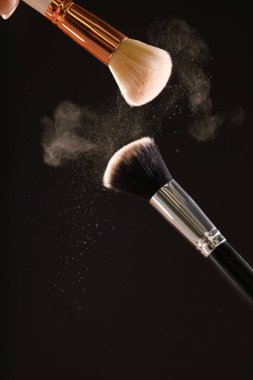 Siyah arka plan üzerine toz allık patlama ile kozmetik fırçalar makyaj. Cilt Bakımı ya da moda kavramı.