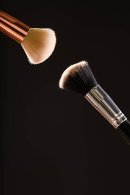 Siyah arka plan üzerine toz allık patlama ile kozmetik fırçalar makyaj. Cilt Bakımı ya da moda kavramı.