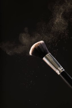 Siyah arka plan üzerine toz allık patlama ile kozmetik fırçalar makyaj. Cilt Bakımı ya da moda kavramı.