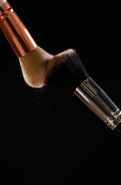 Siyah arka plan üzerine toz allık patlama ile kozmetik fırçalar makyaj. Cilt Bakımı ya da moda kavramı.