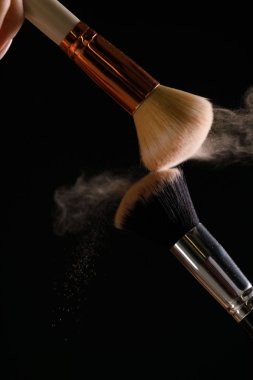 Siyah arka plan üzerine toz allık patlama ile kozmetik fırçalar makyaj. Cilt Bakımı ya da moda kavramı.