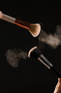 Siyah arka plan üzerine toz allık patlama ile kozmetik fırçalar makyaj. Cilt Bakımı ya da moda kavramı.