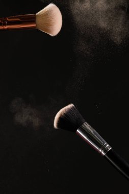 Siyah arka plan üzerine toz allık patlama ile kozmetik fırçalar makyaj. Cilt Bakımı ya da moda kavramı.