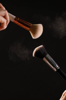 Siyah arka plan üzerine toz allık patlama ile kozmetik fırçalar makyaj. Cilt Bakımı ya da moda kavramı.