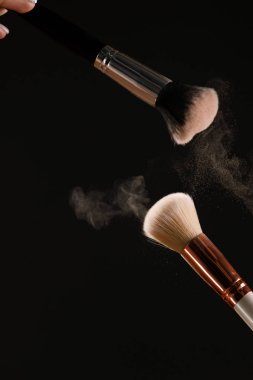 Siyah arka plan üzerine toz allık patlama ile kozmetik fırçalar makyaj. Cilt Bakımı ya da moda kavramı.