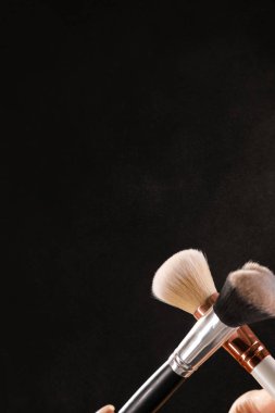 Siyah arka plan üzerine toz allık patlama ile kozmetik fırçalar makyaj. Cilt Bakımı ya da moda kavramı.