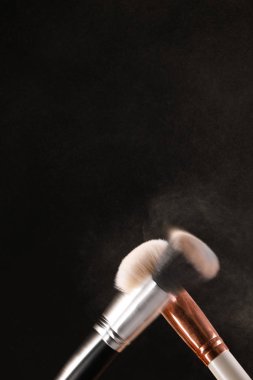 Siyah arka plan üzerine toz allık patlama ile kozmetik fırçalar makyaj. Cilt Bakımı ya da moda kavramı.