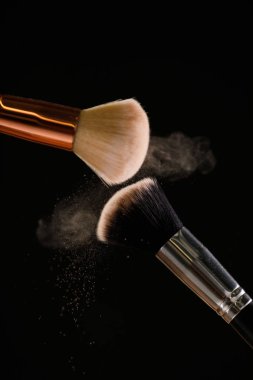 Siyah arka plan üzerine toz allık patlama ile kozmetik fırçalar makyaj. Cilt Bakımı ya da moda kavramı.