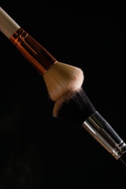 Siyah arka plan üzerine toz allık patlama ile kozmetik fırçalar makyaj. Cilt Bakımı ya da moda kavramı.