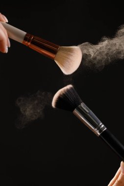 Siyah arka plan üzerine toz allık patlama ile kozmetik fırçalar makyaj. Cilt Bakımı ya da moda kavramı.