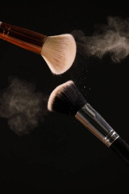 Siyah arka plan üzerine toz allık patlama ile kozmetik fırçalar makyaj. Cilt Bakımı ya da moda kavramı.