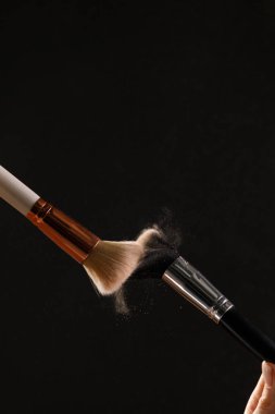 Siyah arka plan üzerine toz allık patlama ile kozmetik fırçalar makyaj. Cilt Bakımı ya da moda kavramı.