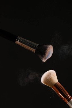 Siyah arka plan üzerine toz allık patlama ile kozmetik fırçalar makyaj. Cilt Bakımı ya da moda kavramı.