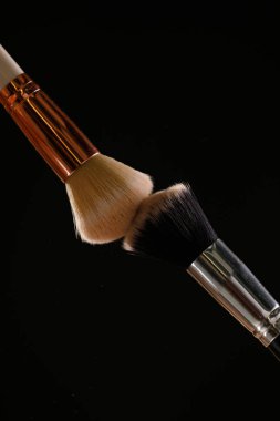 Siyah arka plan üzerine toz allık patlama ile kozmetik fırçalar makyaj. Cilt Bakımı ya da moda kavramı.