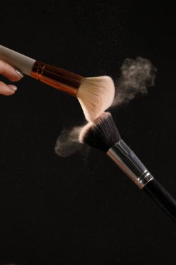 Siyah arka plan üzerine toz allık patlama ile kozmetik fırçalar makyaj. Cilt Bakımı ya da moda kavramı.