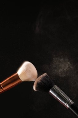 Siyah arka plan üzerine toz allık patlama ile kozmetik fırçalar makyaj. Cilt Bakımı ya da moda kavramı.