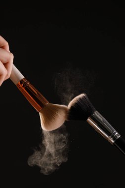 Siyah arka plan üzerine toz allık patlama ile kozmetik fırçalar makyaj. Cilt Bakımı ya da moda kavramı.