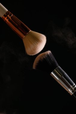 Siyah arka plan üzerine toz allık patlama ile kozmetik fırçalar makyaj. Cilt Bakımı ya da moda kavramı.