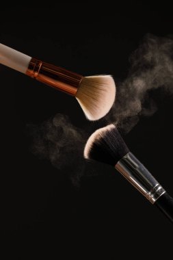 Siyah arka plan üzerine toz allık patlama ile kozmetik fırçalar makyaj. Cilt Bakımı ya da moda kavramı.