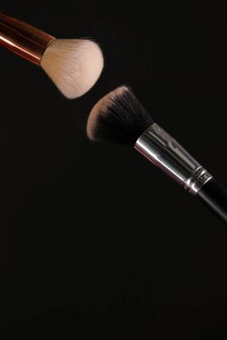 Siyah arka plan üzerine toz allık patlama ile kozmetik fırçalar makyaj. Cilt Bakımı ya da moda kavramı.