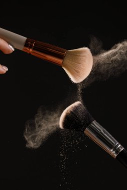 Siyah arka plan üzerine toz allık patlama ile kozmetik fırçalar makyaj. Cilt Bakımı ya da moda kavramı.