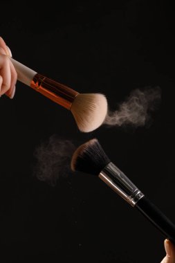 Siyah arka plan üzerine toz allık patlama ile kozmetik fırçalar makyaj. Cilt Bakımı ya da moda kavramı.