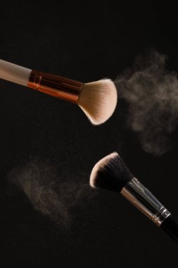 Siyah arka plan üzerine toz allık patlama ile kozmetik fırçalar makyaj. Cilt Bakımı ya da moda kavramı.